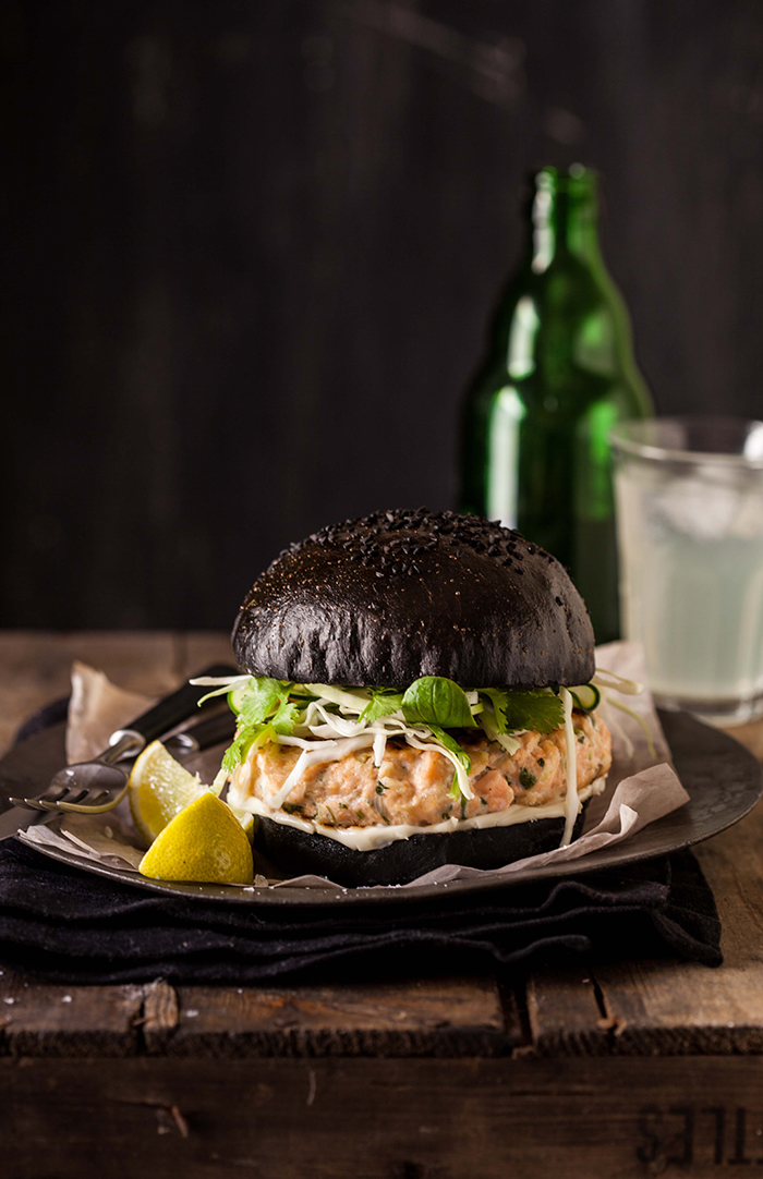 salmon burger on a black brioche bun with crunchy greens
