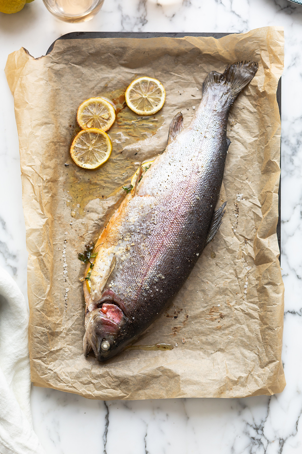 A whole roasted rainbow trout on a baking tray with roasted lemon