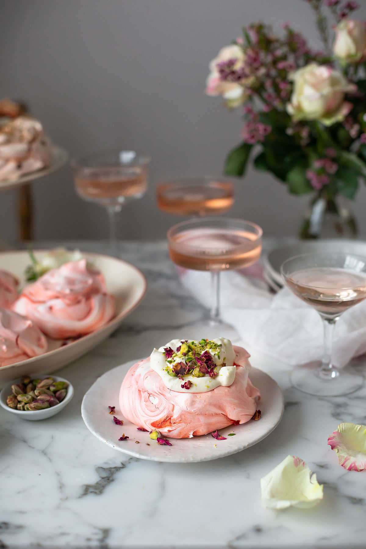 a plate with rose meringues, fresh cream and pistachios