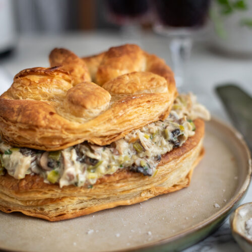 Layered puff pastry with creamy chicken pie filling on a plate, wine glass blurred in the background, serving dish visible