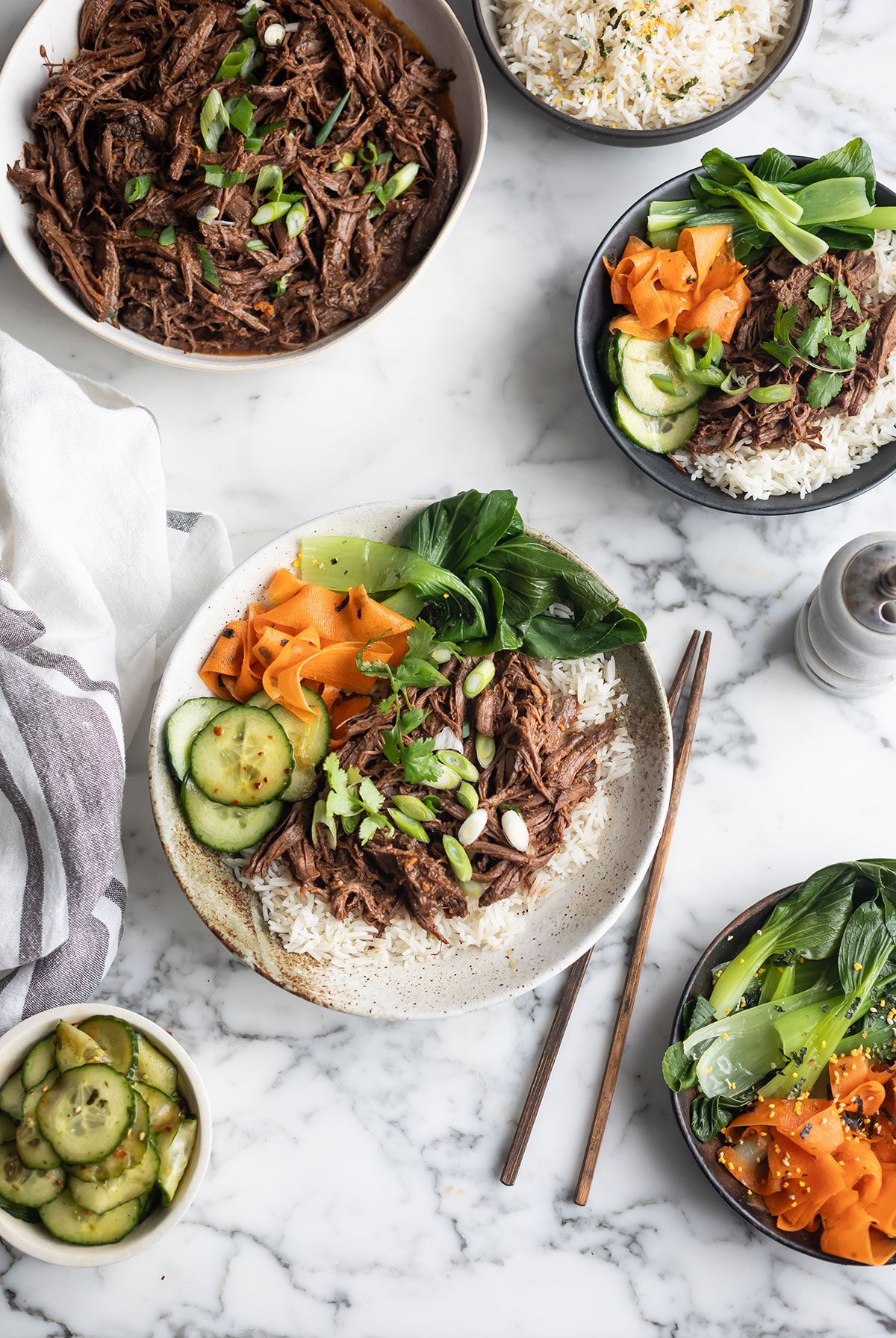 Top-down view of beef bowls with shredded slow-cooked Korean beef, white rice, and assorted veggies on a marble surface.